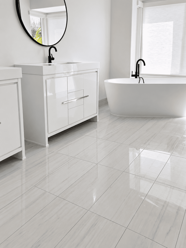 Elegant bathroom with white tile flooring, bathtub, and vanity with mirror.