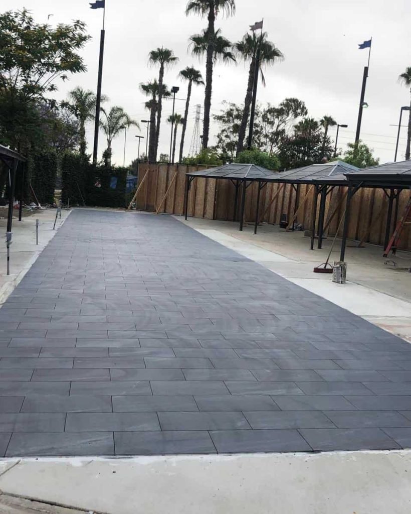Commercial outdoor tile walkway with shade structures and palm trees in background.