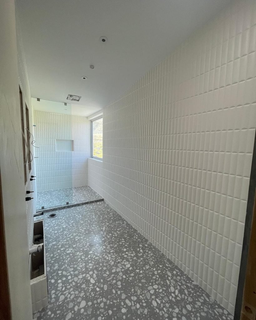 Modern bathroom with white tiled walls and terrazzo flooring under construction.